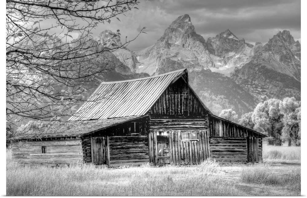 Black and white photo of an old barn in a field with the Grand Teton mountain range in the distance.