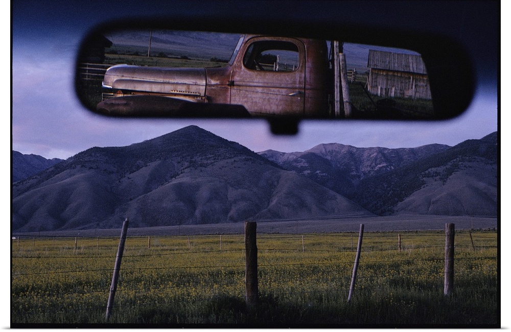 An old truck and barn are reflected in a rear-view mirror.