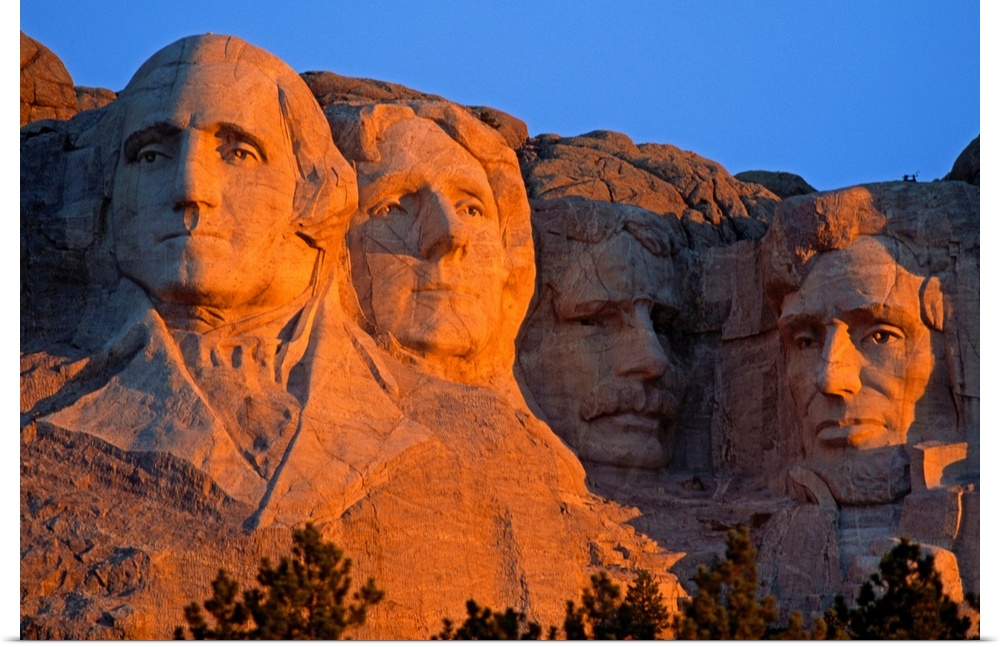 A picture taken of Mount Rushmore as the sun begins to set and shines on the faces in the mountain.