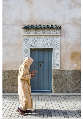 A man wearing a djellaba walks past a decorative doorway in the medina (old town)