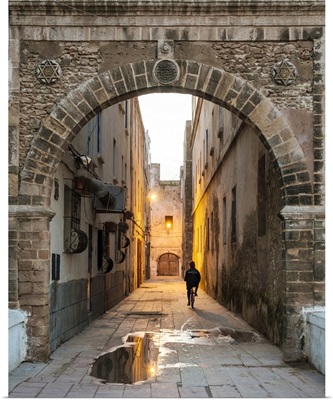 A person rides a bicycle through a dark alley in the medina old town at dawn