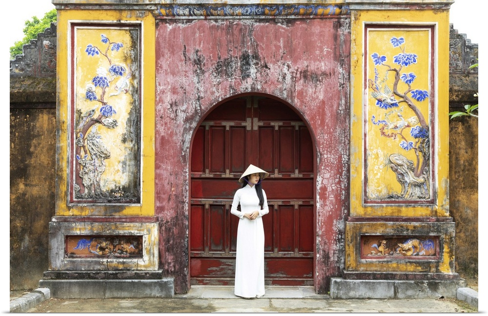 A Vietnamese girl in an Ao Dai dress stands in front of a historical gate in Hue Imperial Citadel, Hue, Thua Thien-Hue pro...