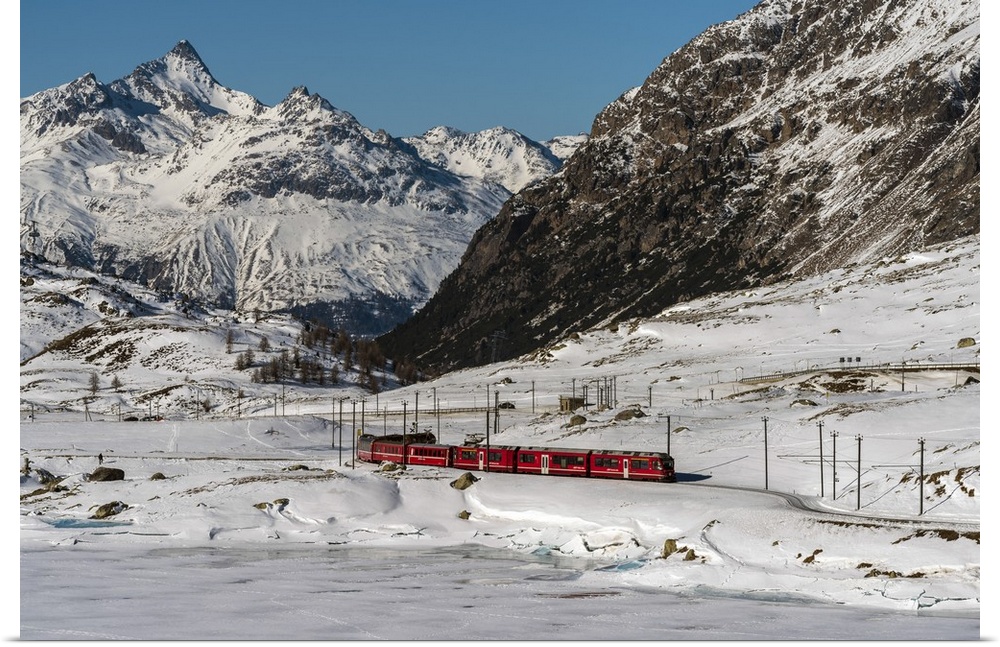 The famous Bernina Express red train passing Lago Bianco in a scenic winter mountain landscape, Graubunden, Switzerland