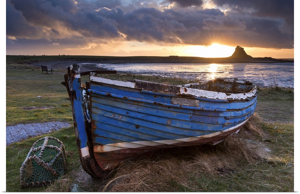 Decaying fishing boat on Holy Island at dawn, with Lindisfarne Castle beyond, Northumberland, England. Spring (March)