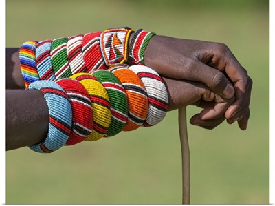 Kenya, A Samburu warrior with beaded bracelets rests his hands on a walking stick