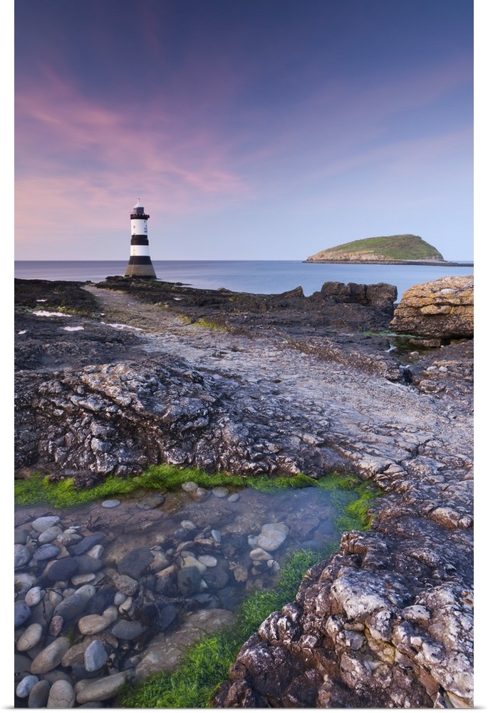 Twilight on the rocky Anglesey coast looking towards Penmon Point Lighthouse and Puffin Island, Anglesey, North Wales, UK....