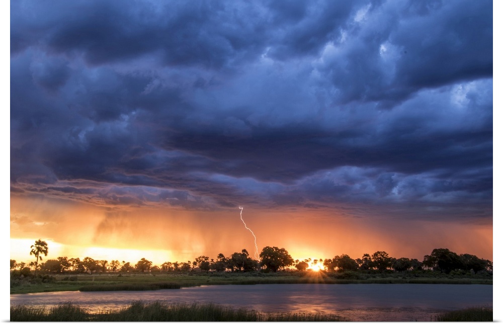Lightning shoots from a summer thunderstorm as the sun sets behind it, Okavango Delta, Botswana