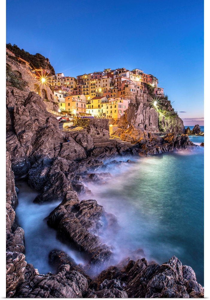 Manarola village illuminated by the blue light of dusk with its typical pastel colored houses. Cinque Terre National Park....