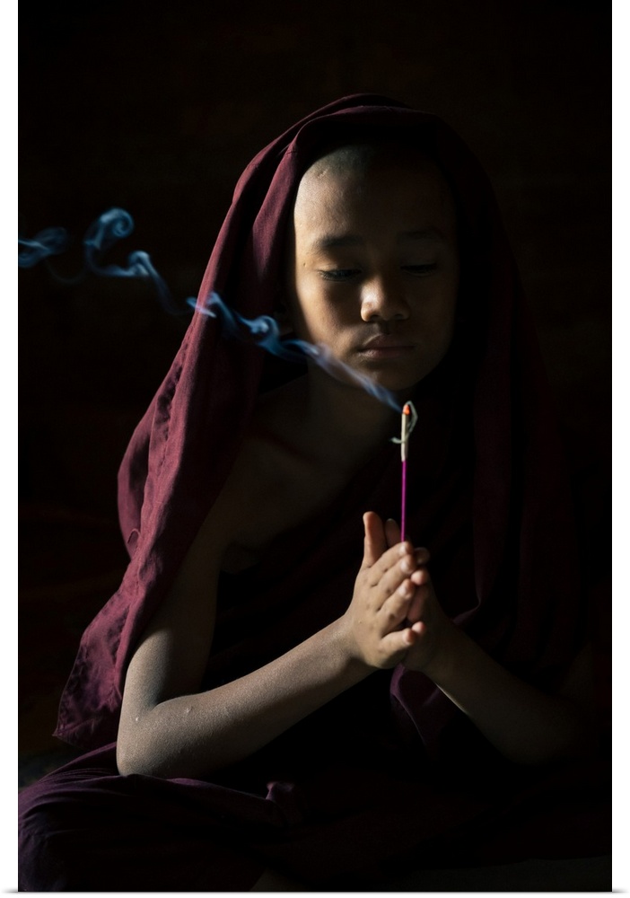 Novice monk holding a lit incense stick while praying inside a temple, UNESCO, Bagan, Mandalay Region, Myanmar