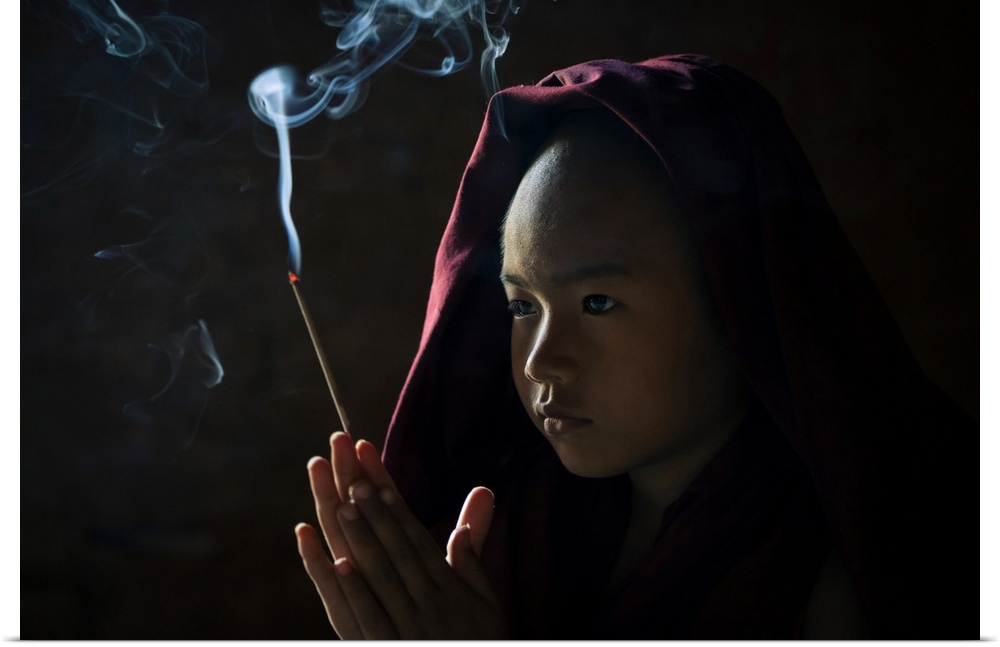 Novice monk holding a lit incense stick while praying inside a temple, UNESCO, Bagan, Mandalay Region, Myanmar