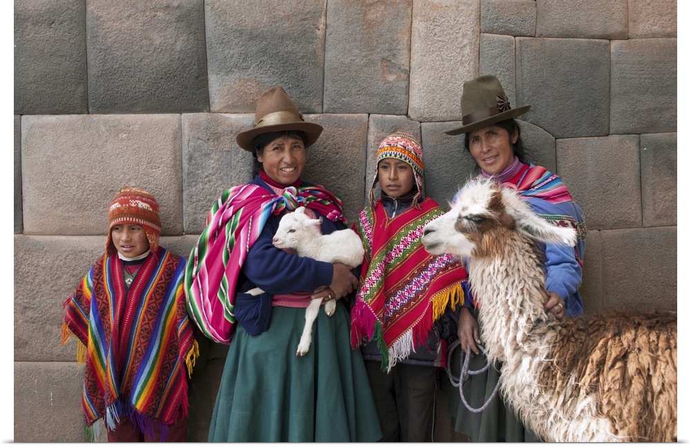 South America, Peru, Cusco. Quechua people standing in front of an Inca wall, holding a lamb and a llama and wearing tradi...
