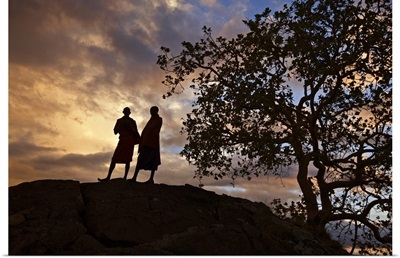 Two Maasai men silhouetted on a hill at sunset