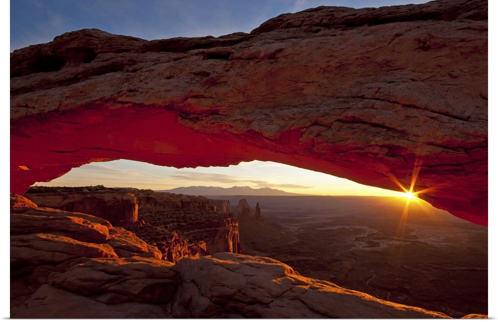 A photograph is taken through the mesa arch as the sun begins to rise over the horizon.