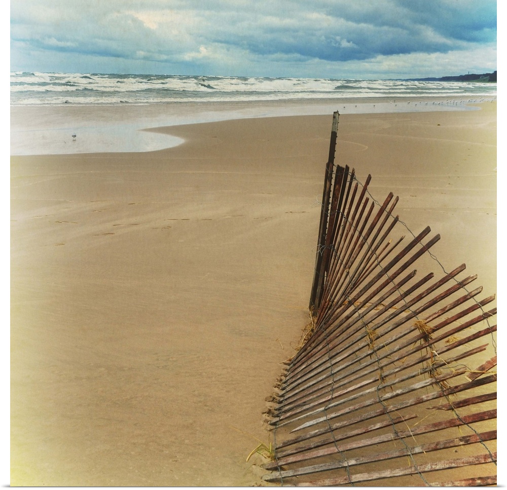 A worn down wooden fence on a sandy beach at low tide.
