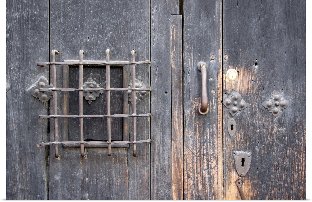 Oversized, horizontal close up photograph of an old wooden door with elaborate safe opening and decorative metal fixtures.