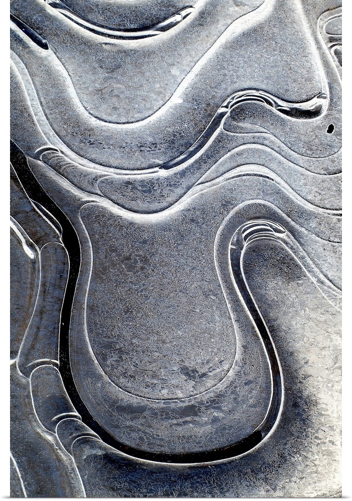 This is a fine art photograph of curving shapes and monochromic sheens of bright to dark on a vertical wall hanging.