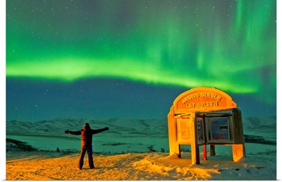 A man looks in awe at the northern lights near the Arctic Circle sign