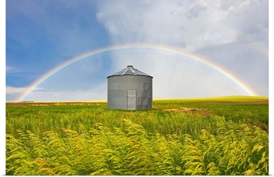 A rainbow over a grain silo and wheat field after a thunderstorm