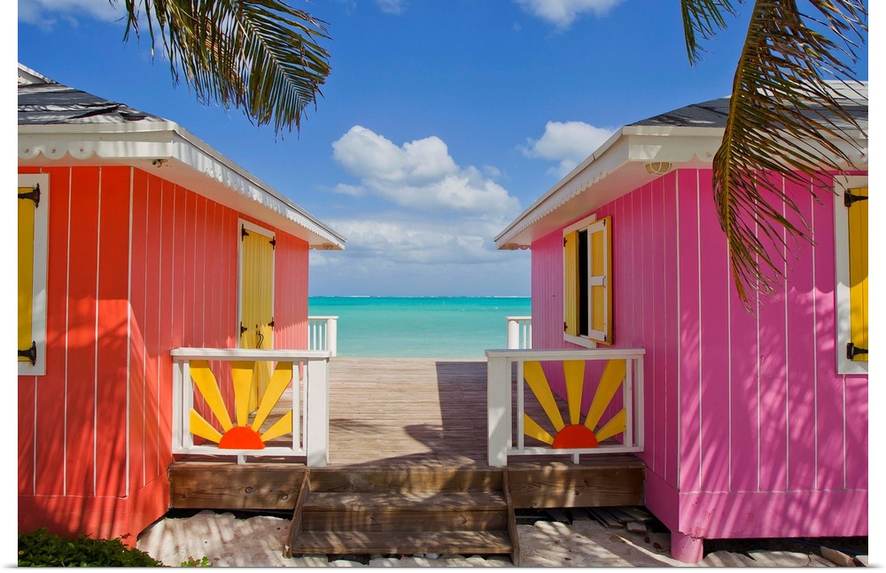 Two colorful cabanas sit on the beach and have a small walking path in between that leads down to the water.