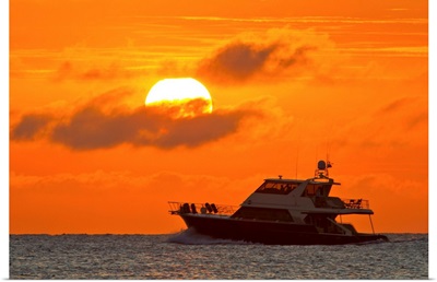 Boat passing in front of a big glowing sun during a spectacular sunset