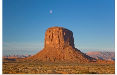 Moon visible over rock formation in Monument Valley in early morning