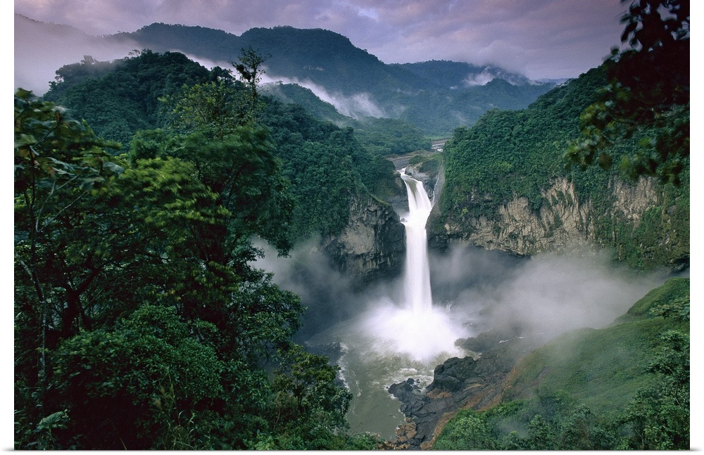 Photograph of waterfall surrounded by rainforest with mountain silhouette in the distance.
