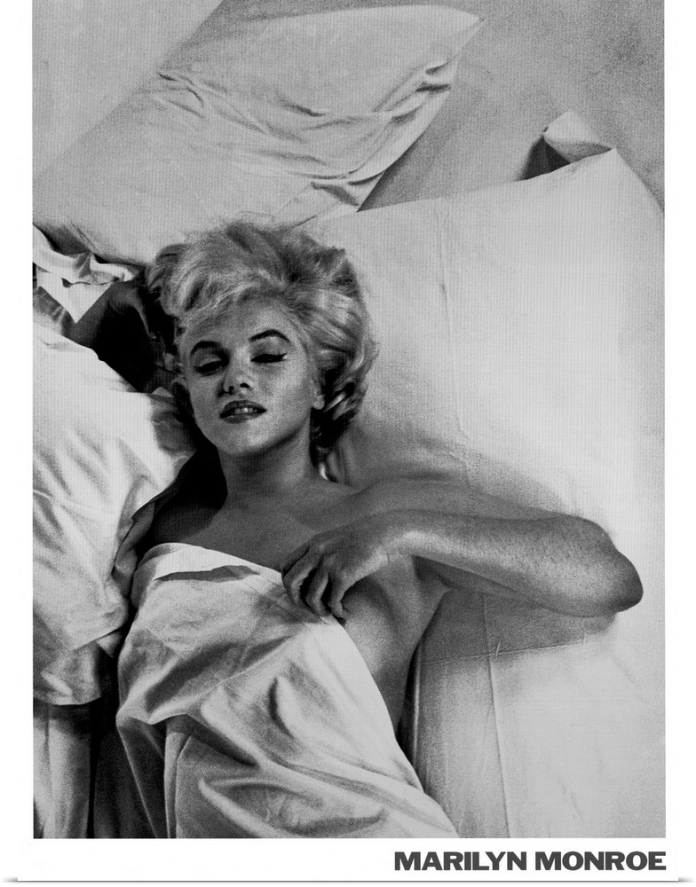 Large monochromatic photograph shows a famous American actress, model, and singer laying in bed with a blanket over her nu...