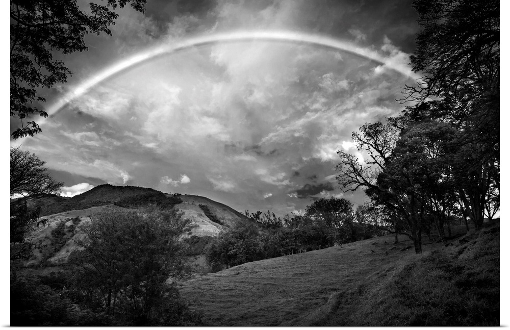 Black and white photograph of a wilderness landscape with a large rainbow in the sky.