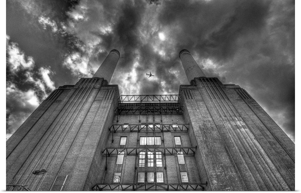 A black and white photograph looking up at a power station with dramatic clouds above.