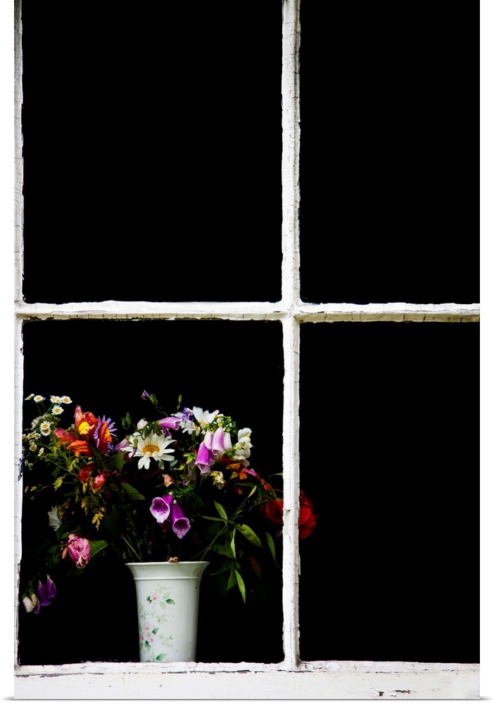 An old white window frame with a white vase filled with a jumble of cottage garden flowers.