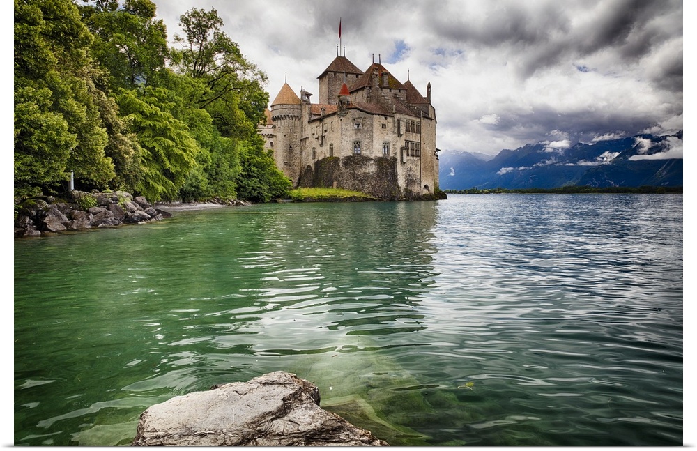 The Chateau de Chillon on the edge of Lake Geneva, with the Alps in the distance on a cloudy day, Switzerland.