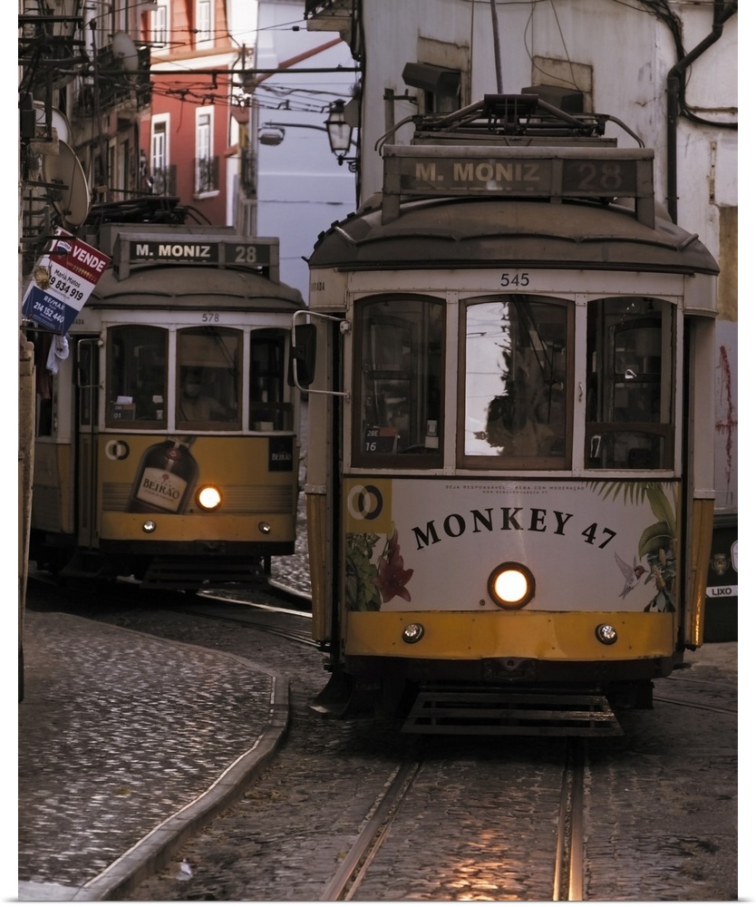 Vintage trams of line 28 traveling in a narrow street in Alfama district of Lisbon at dusk, Portugal, Europe.