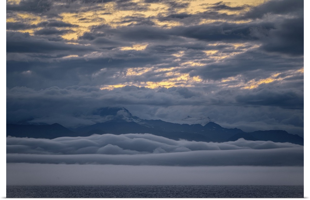 Peaceful snow-capped Alaskan mountain range at ocean's edge with clouds above and clouds below (cloud inversion) make for ...