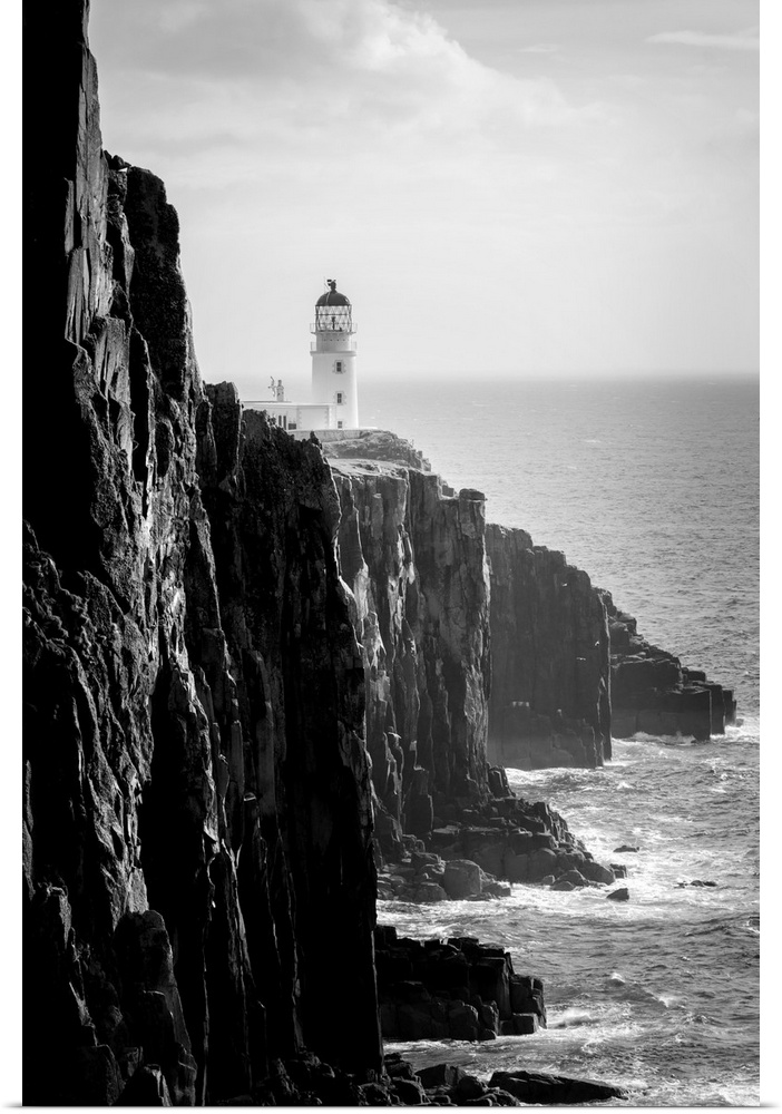 Fine art photo of a lighthouse at the edge of a cliff by the ocean in black and white.