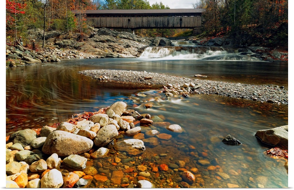A rocky riverbed in New Hampshire with the Swiftwater Covered Bridge in the distance.