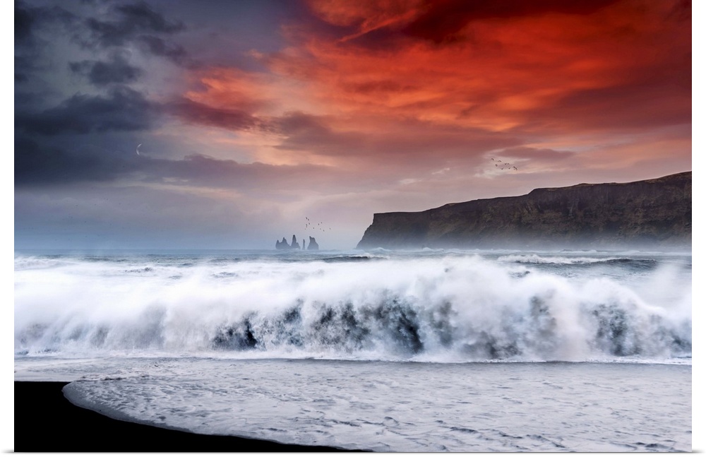 Photograph of a large crashing wave onto the shore with a bold red sunset above and a crescent moon to the left.