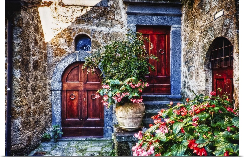 Two wooden doors in a stone wall surrounded by blooming potted flowers.