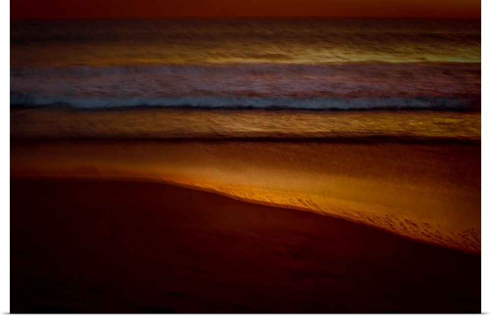 Golden lit photograph of ocean waves rolling on to the beach shore with a blurred look, created with a long exposure.