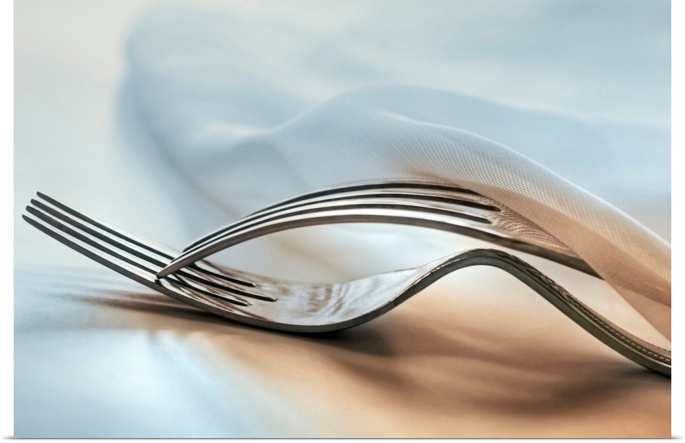 In this close up photograph two forks lie on top of each other under a napkin on a table.