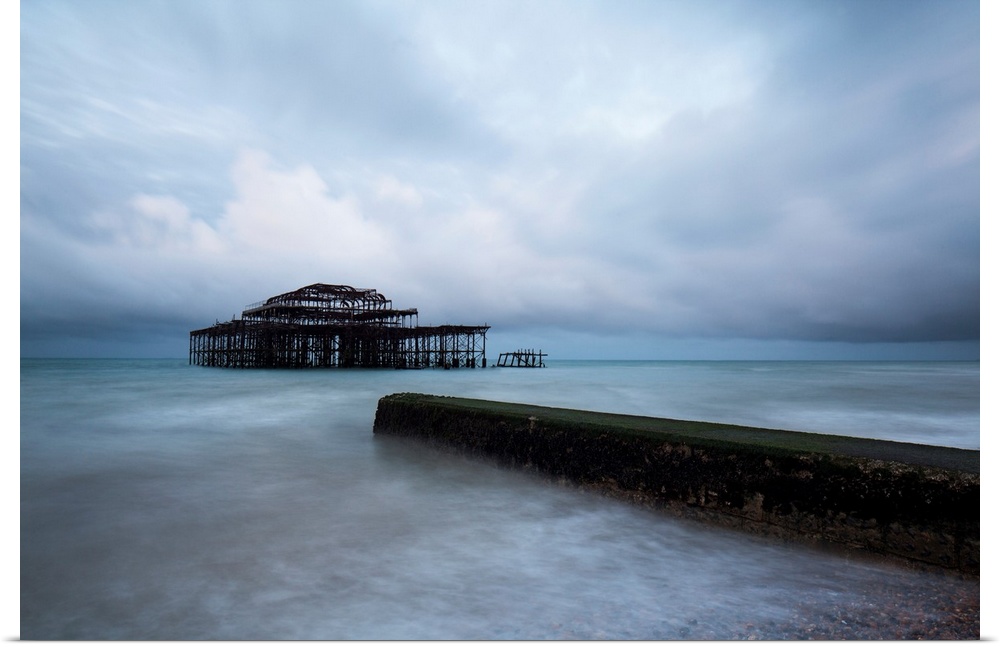 A cool blue dramatic storm image of Brighton Pier, Sussex, UK with the Old Pier in stormy seas and a concrete jetty in the...