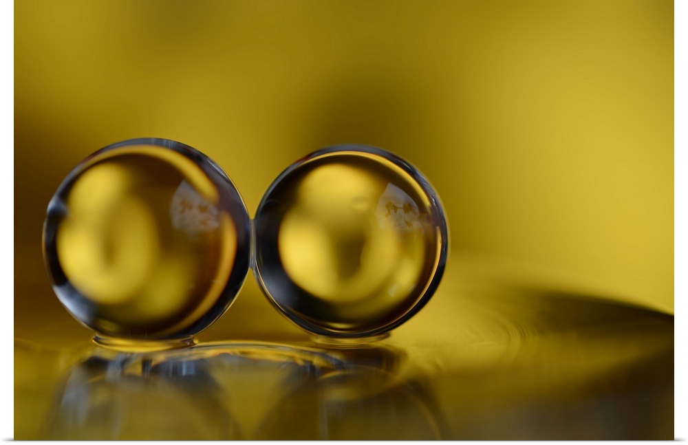 Macro photograph of two water drops side by side and reflecting onto the yellow surface below them.