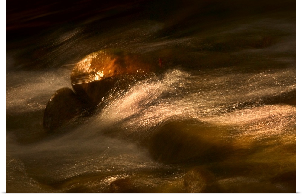 Photograph taken of rushing water gliding over rocks that are touched by spots of sunlight.