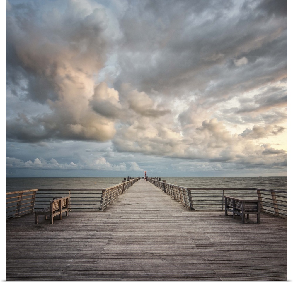 A wooden pier leading to the ocean with dramatic clouds above.