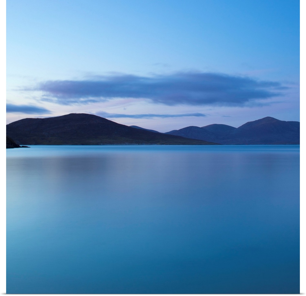 A cool blue minimal zen-like seascape of flat calm water with silhouetted mountains.
