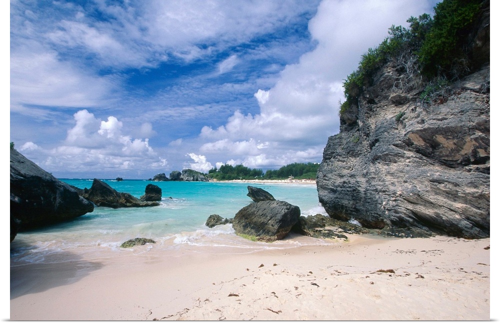 Big photograph displays a secluded portion of a sandy beach in Horseshoe Bay, Bermuda on a sunny day.  The rough and giant...