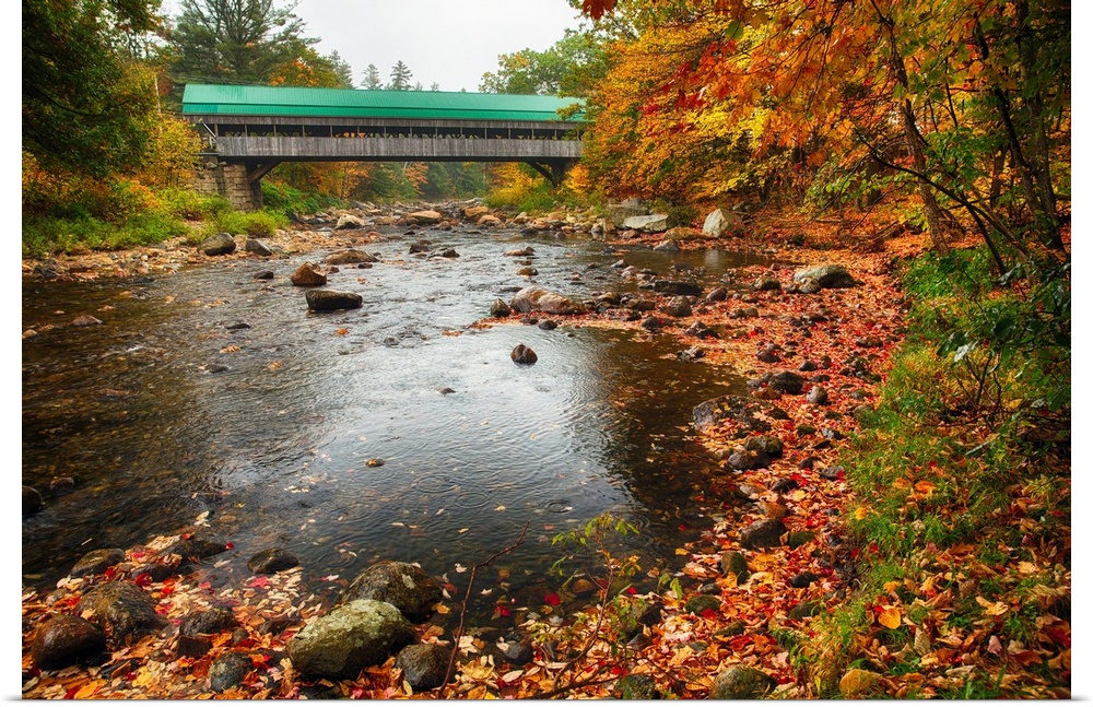 A covered bridge with a colorful roof stretching over the Ellis River in New Hampshire.