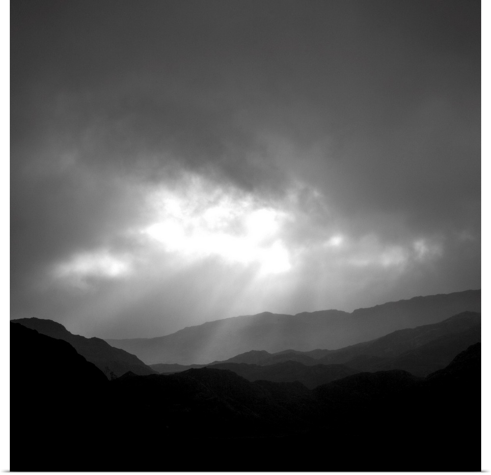 An uplifting monochromatic image of God's Crepuscular Rays bursting through clouds over silhoutted muntains.