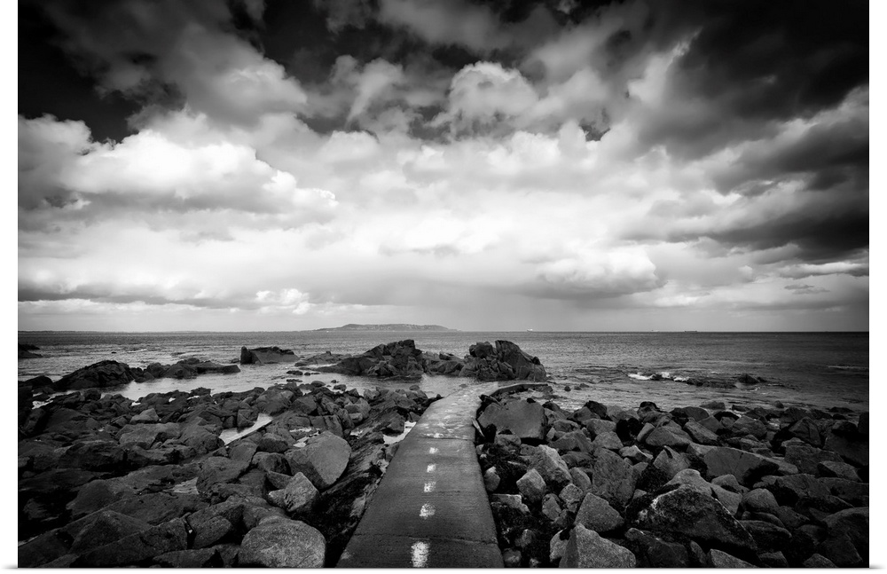 Black and white photograph of a road surrounded by coastal rocks leading into the ocean.