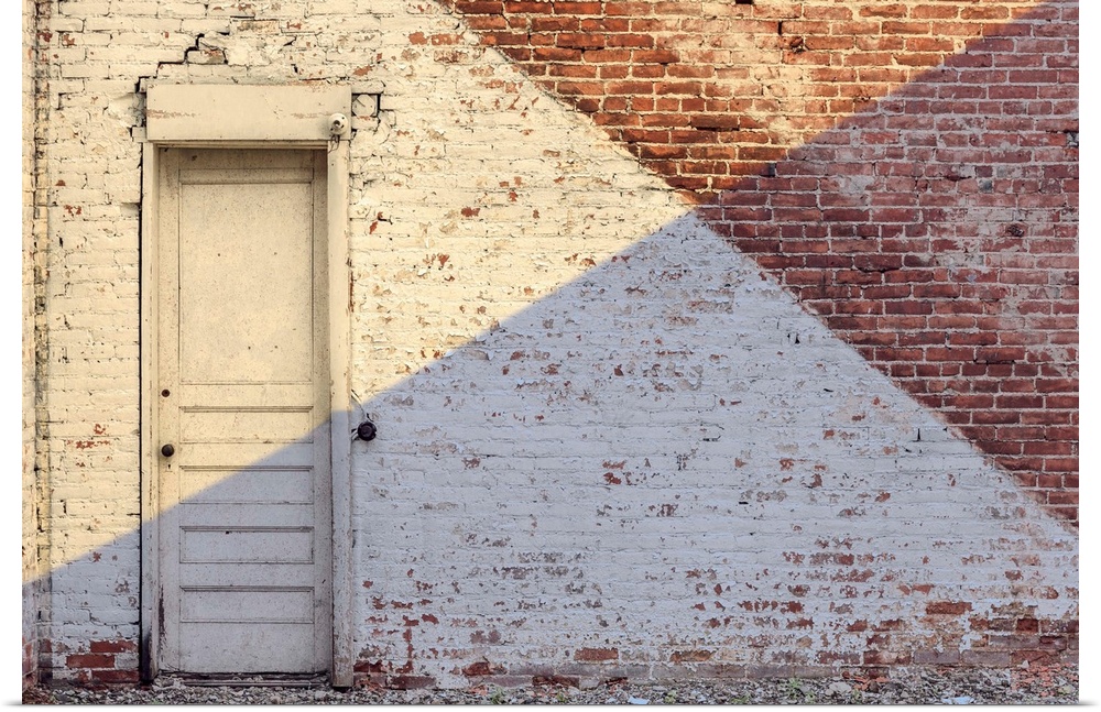 Photograph of an aged brick wall with a white door, angled paint lines, and an angled shadow on half of the image.