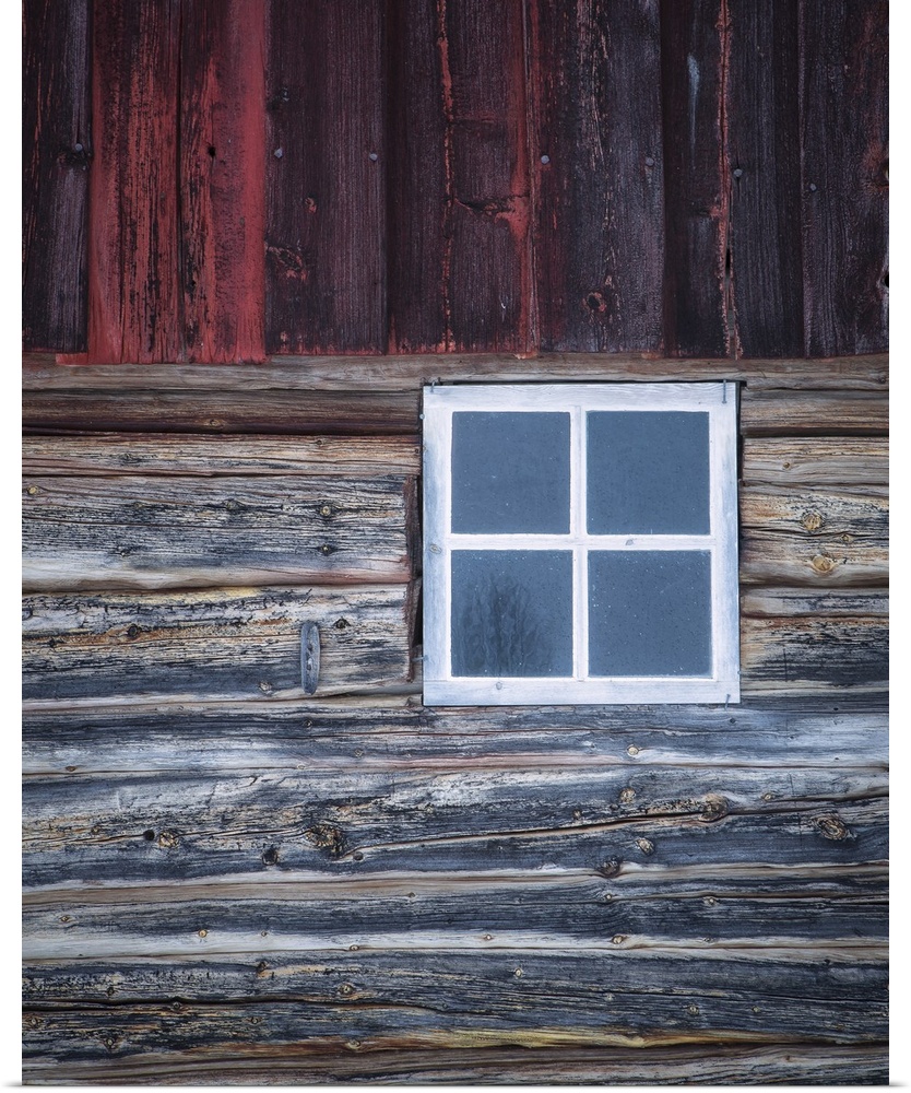 A close-up of an old white window ina weather Norweigian wooden building in the snow with grey and deep red timbers.